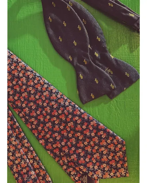 Floral print necktie and embroidered navy bow tie displayed on a green background – men’s tie styles for the Kentucky Derby.