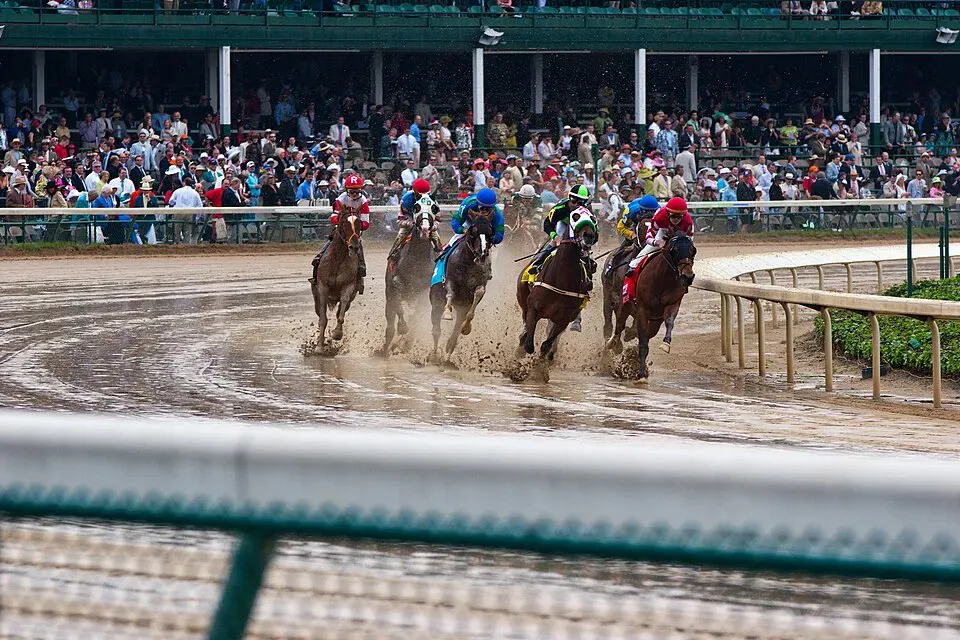 Horses racing on a muddy Churchill Downs track in the rain, with crowds watching from the stands during the Kentucky Derby.