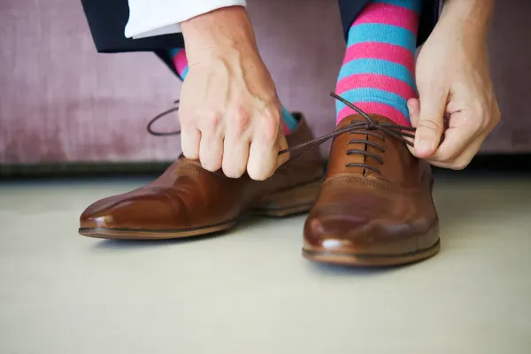 Close-up of a man tying brown dress shoes, wearing bright pink and blue striped socks – men’s Derby Day style and sock guide.