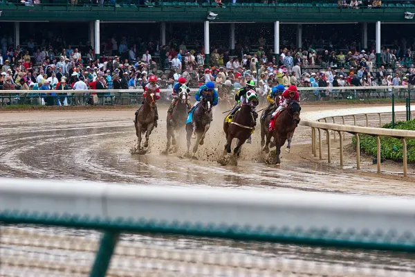 Horses racing on a muddy Churchill Downs track in the rain, with crowds watching from the stands during the Kentucky Derby.